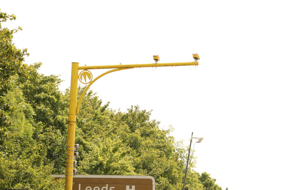 Yellow average speed camera poles beside a UK road, the kind left running through empty roadworks
