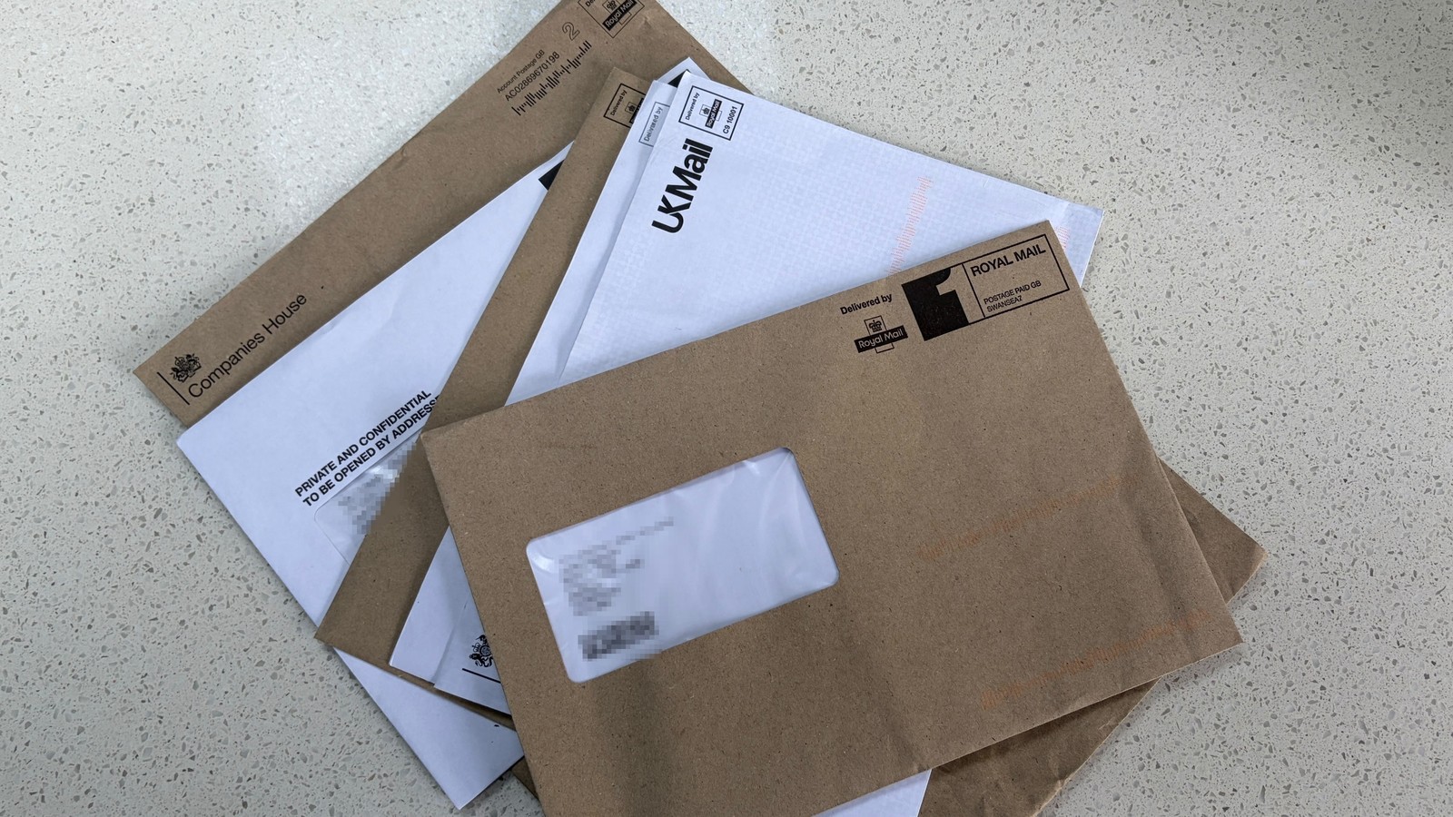 Five official envelopes stacked on a kitchen counter, personal details hidden
