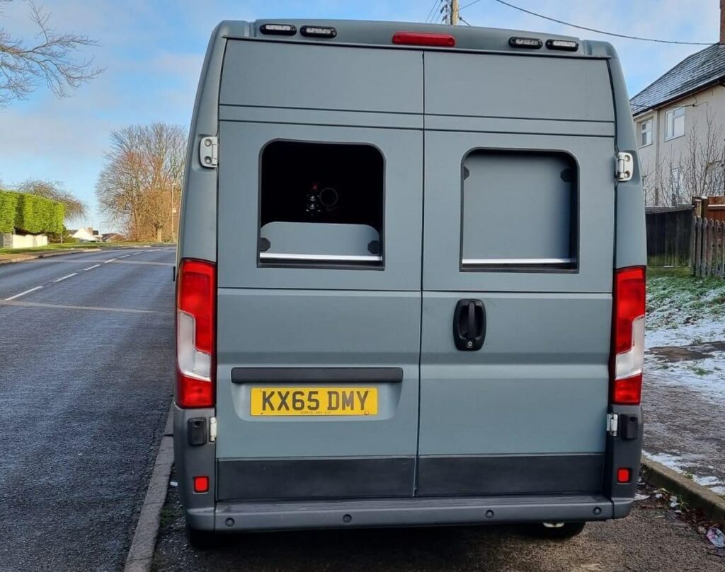An unmarked grey speed camera van parked at the roadside, camera visible through the rear window