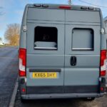 An unmarked grey speed camera van parked at the roadside, camera visible through the rear window